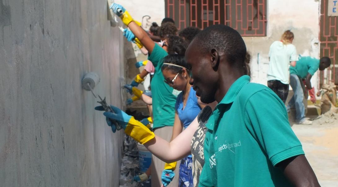 A Projects Abroad staff member helps with painting during construction volunteer work abroad. A staff member supports volunteers as they paint a newly constructed wall on one of our volunteer building projects